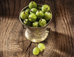 Juicy gooseberries in metal bowl on vintage wood background
