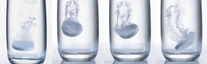 Tablets Falling and Dissolving into a Glass of Water against White Background