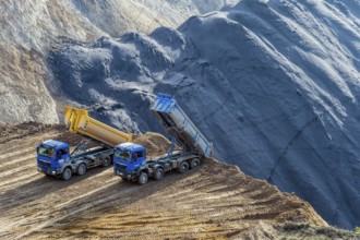 2 dumper trucks stand at the edge of the open-cast mine and tip over a hole