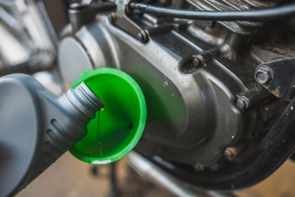 A close-up of a motorcycle engine with oil being poured through a green funnel