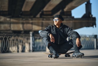 Skater male relax sitting on skateboard on street urban background. Extreme sports concept