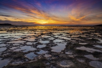 A beautiful sunset over the ocean with rocky beach and tidal pools in the foreground
