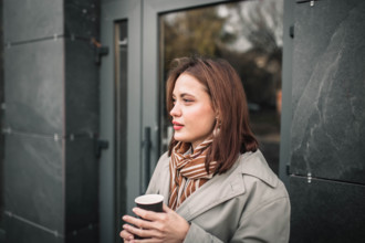 Side profile of a woman in a coat and scarf, holding a cup outside