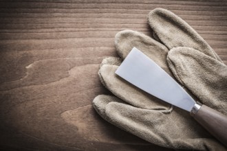 Paint scraper and safety glove on wooden board