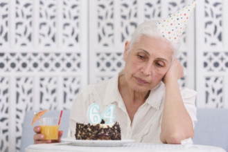 Unhappy elder woman looking her birthday cake holding glass juice hand