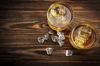 Two glasses with ice and whiskey on wooden background (top view)