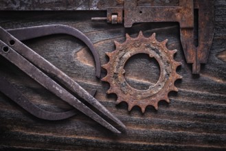 Rusted antique measuring calipers with cog- wheel on vintage dark wooden background close up view