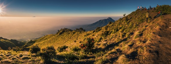 Panoramic photo of mountains surrounding Mount Merbabu and hikers at top during sunrise near Yogya