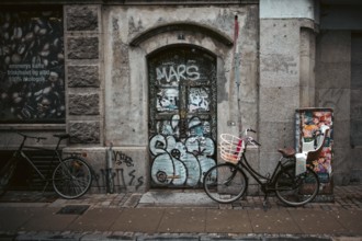 Urban street scene with bicycles and a graffiti-covered door against a weathered brick wall in