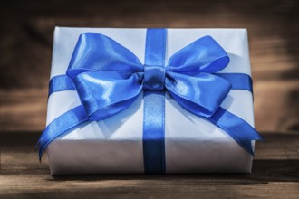 White giftbox with blue ribbon on vintage wood
