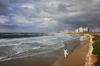 Storm cloud hanging over the sea, the woman in white performs asana Tree on one leg. Promenade and