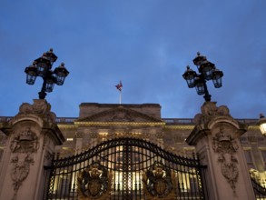 Iron gate with coat of arms and lanterns, illuminated at night in front of a building, London,