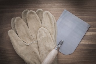 Working safety gloves and bricklaying trowel on vintage wooden background