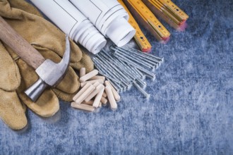 Blueprint rolls claw hammer safety gloves wooden meter metal nails and dowels on scratched metallic