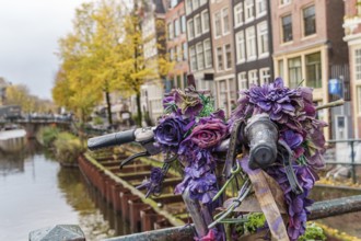 Decorated bicycle with purple flowers on a bridge in an urban environment, Amsterdam, Netherlands
