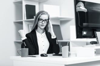 Young pretty business woman sitting at the desk with computer in blue office