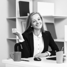 Young pretty business woman sitting at the desk with computer in blue office