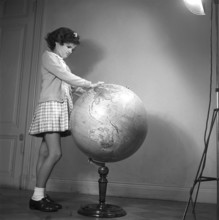 School in the 1940s. A girl in is very closely studying the details of a globe, something is