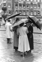 Umbrellas in the 1950s. A group of elderly women are standing together under their umbrellas. It's