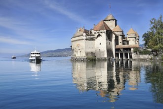 World-wide well-known Château de Chillon on Lake Geneva. The white tourist motor ship floats by a