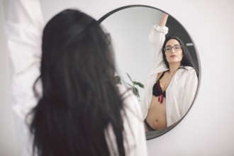 Beautiful young woman in underwear looking at mirror in morning at home. Young woman looking