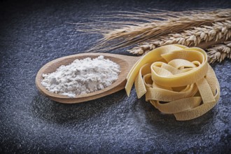Wheat rye ears wooden spoon flour pasta on black background