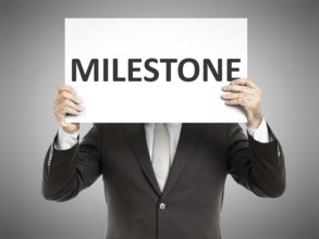 A business man holding a paper in front of his face with the text milestone