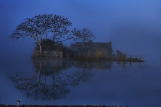 An ancient building a trees reflecting off the waters of a Blue Lake in winters in Ranthambhore