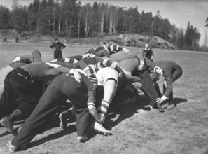 1940s rugby. A group of rugby players are practising on a sunny spring day. The focus is on the
