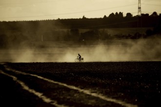 A cyclist rides through the atomised haze of a tractor