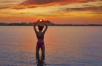 Girl silhouette at sunset heart shape in hands fingers on the beach