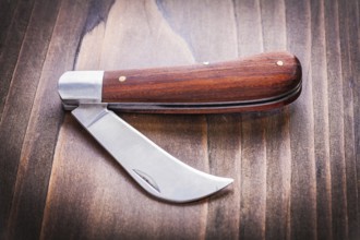 Opened agricultural knife on vintage wooden board close up