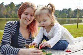 Mother and daughter playing with color shapes game in a park lake
