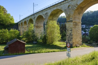 A massive stone viaduct towers over a green landscape with a small country road in the foreground,