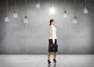 Business woman stands in a gray room with hanging bulbs