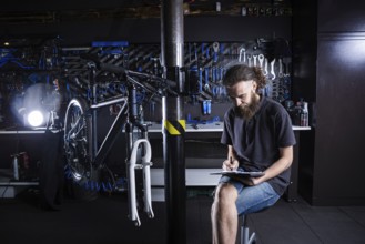 Stylish man with beard, cycle mechanic takes notes, checklist before repairing and servicing bike