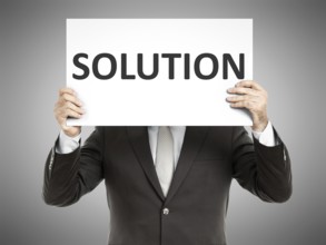 A business man holding a paper in front of his face with the text solution