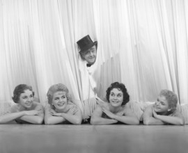 Fun in the 1950s. A gentleman and four ballet dancers at the theatre. He's wearing a top hat when
