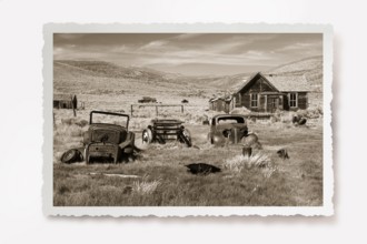 Several rusting car wrecks in a meadow in front of a wooden house in the former gold mining town of