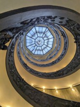 View from below of an ornate spiral staircase with a geometric skylight at the top, showcasing