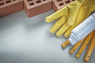 Red bricks safety gloves blueprints wooden meter on concrete background building concept