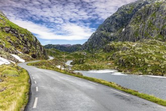 Narrow dangerous mountain road glitters from the rain. The roadside is marked with high poles.