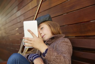 Blond kid girl taking selfie with guitar and winter beret and coat on wooden background
