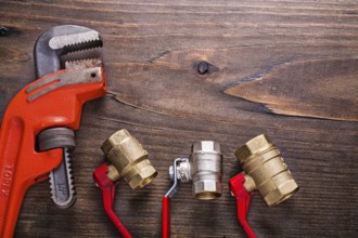Plumbers fixtures with red handles and monkey wrench on vintage wooden board with copyspace