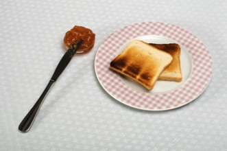 Slice of bread spread with jam and knife on a small bowl