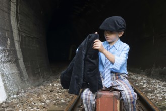 Child in vintage clothes sits on railway road in front of a tunnel