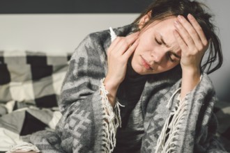Subject disease and treatment. young Caucasian woman sits home bedroom bed wrapped in body blanket