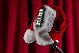 An old retro microphone with a Christmas hat in front of a red velvet background. Austria