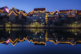 Christmas illuminated house facade of Frohnleiten reflected in the river Mur, blue hour,