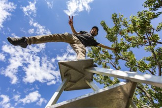 Low angle view of a happy caucasian man on the top of a ladder standing on one leg. as he enjoying